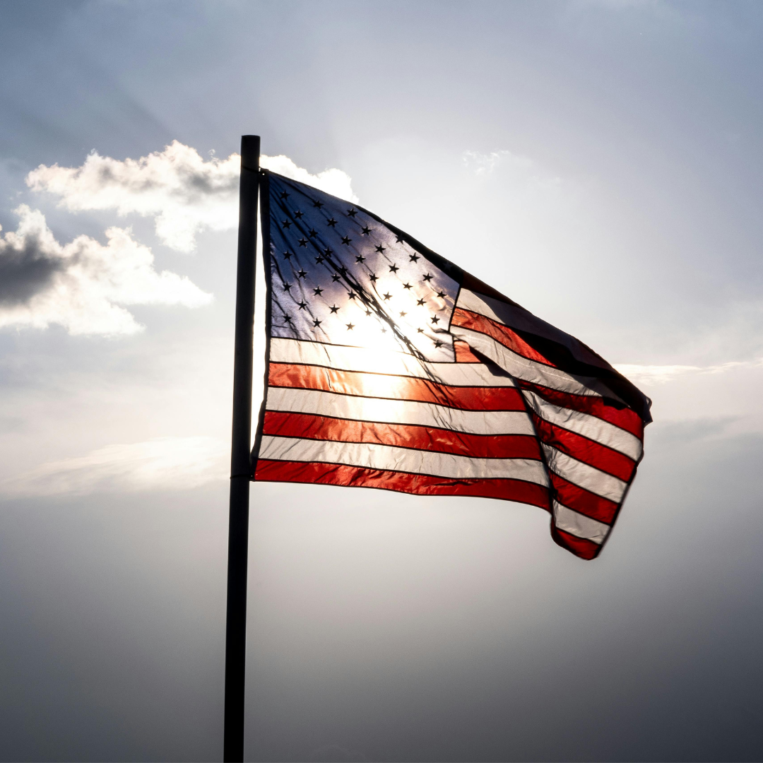An American flag blows in the wind with the sun behind it.