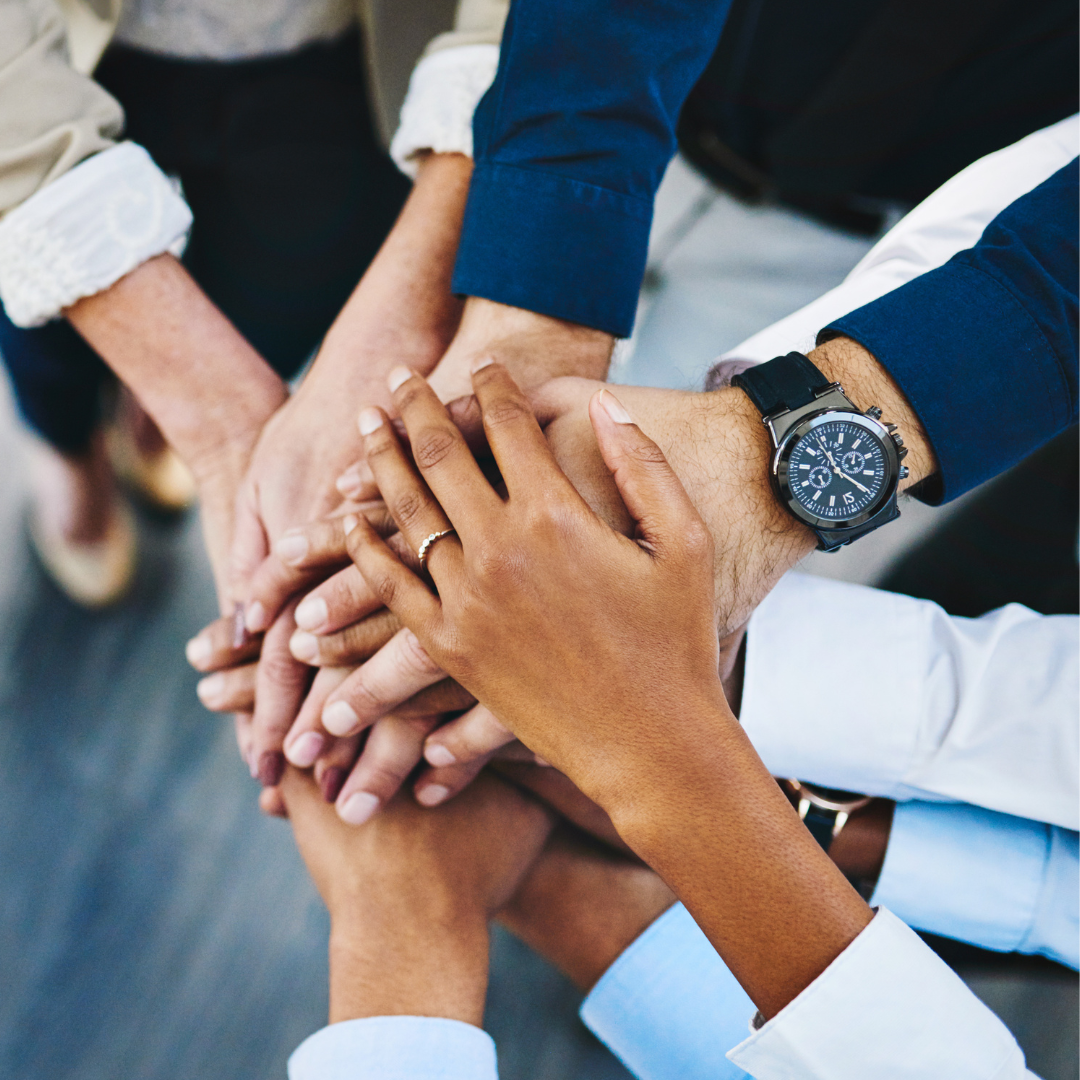 A group of people stack their hands as a form of teamwork, collaboration, and solidarity.