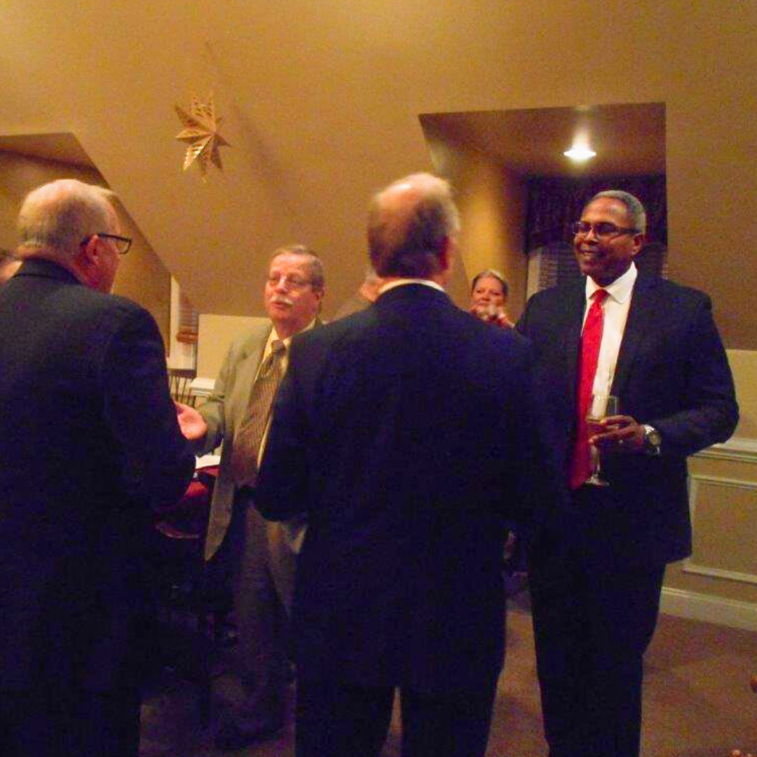 Several members of the NDIA Aberdeen Proving Ground Chapter shake hands and talk at an event.